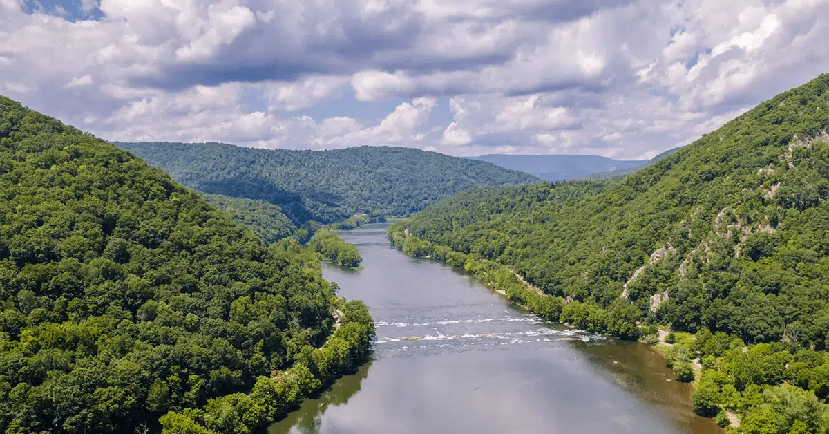 A wide river flows between two tree-covered hills under a partly cloudy sky, with distant forested mountains in the background—an untouched beauty reminiscent of the pristine standards upheld by Cleaning Service Blacksburg.